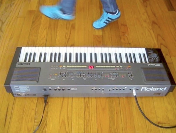 Analog Tara dances in green-blue suede sneakers while activating keys on a Roland HS-60 synth on a wood floor